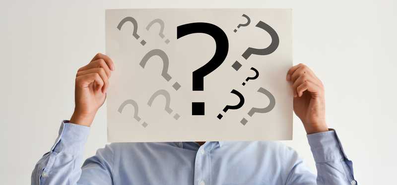 A person conceals their face with a sign covered in question marks.