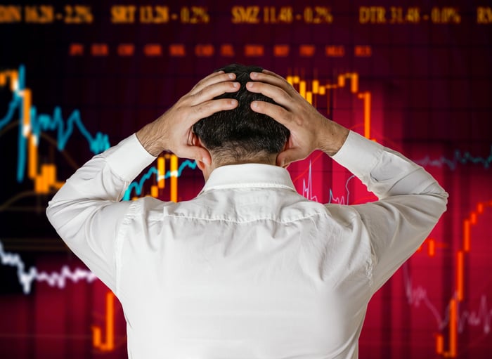 A person holding his head in exasperation while watching falling stock price charts on a display board.