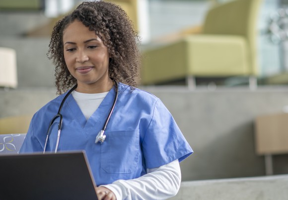 A medical professional performs work tasks on a laptop.