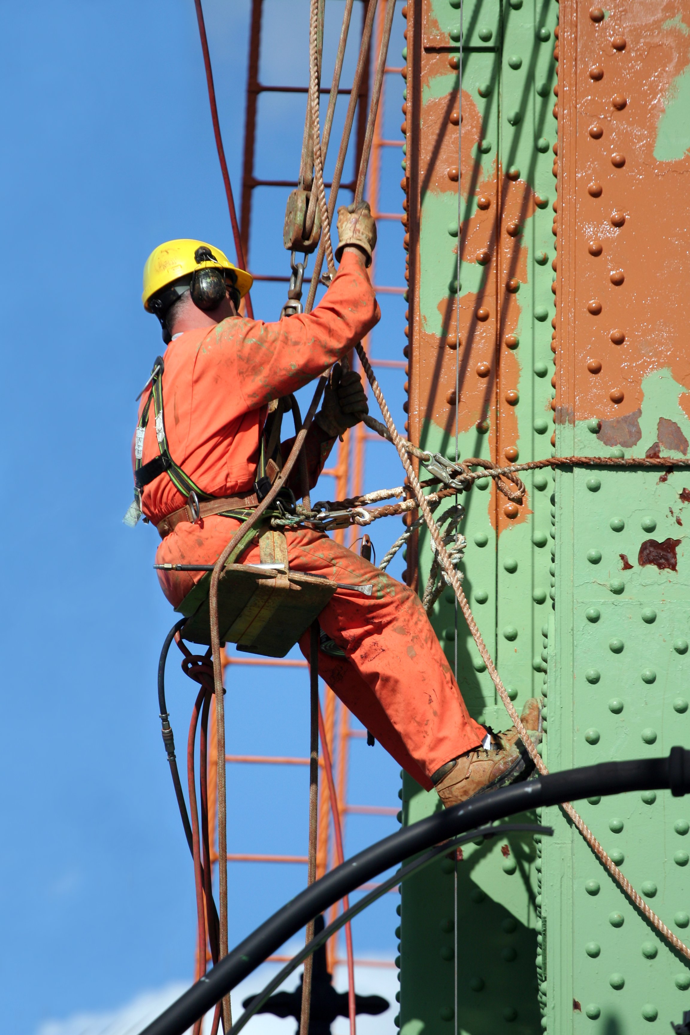 A person is suspended from a bridge, doing maintenance work.