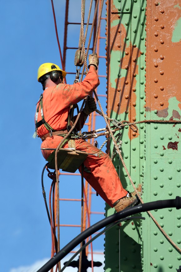 A person is suspended from a bridge, doing maintenance work.