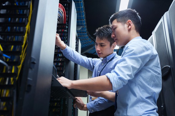 Two technicians working on servers in a data center cabinet.