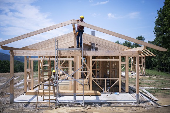 Two people work on a construction site, framing a house.