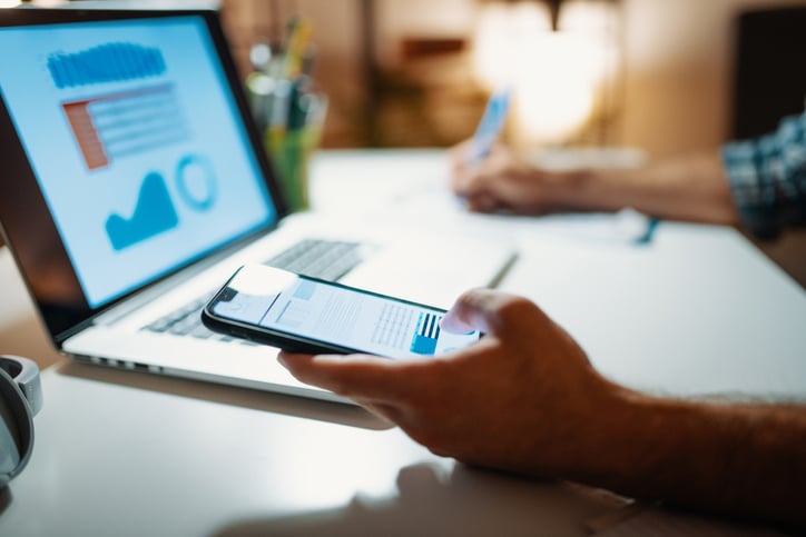 Person holding phone, with laptop on table.