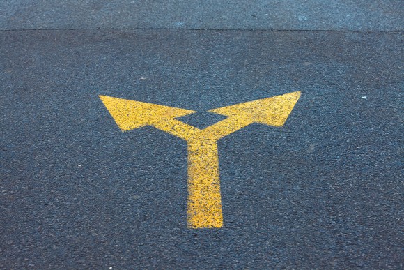 An arrow sign painted on a road diverges in two directions. 