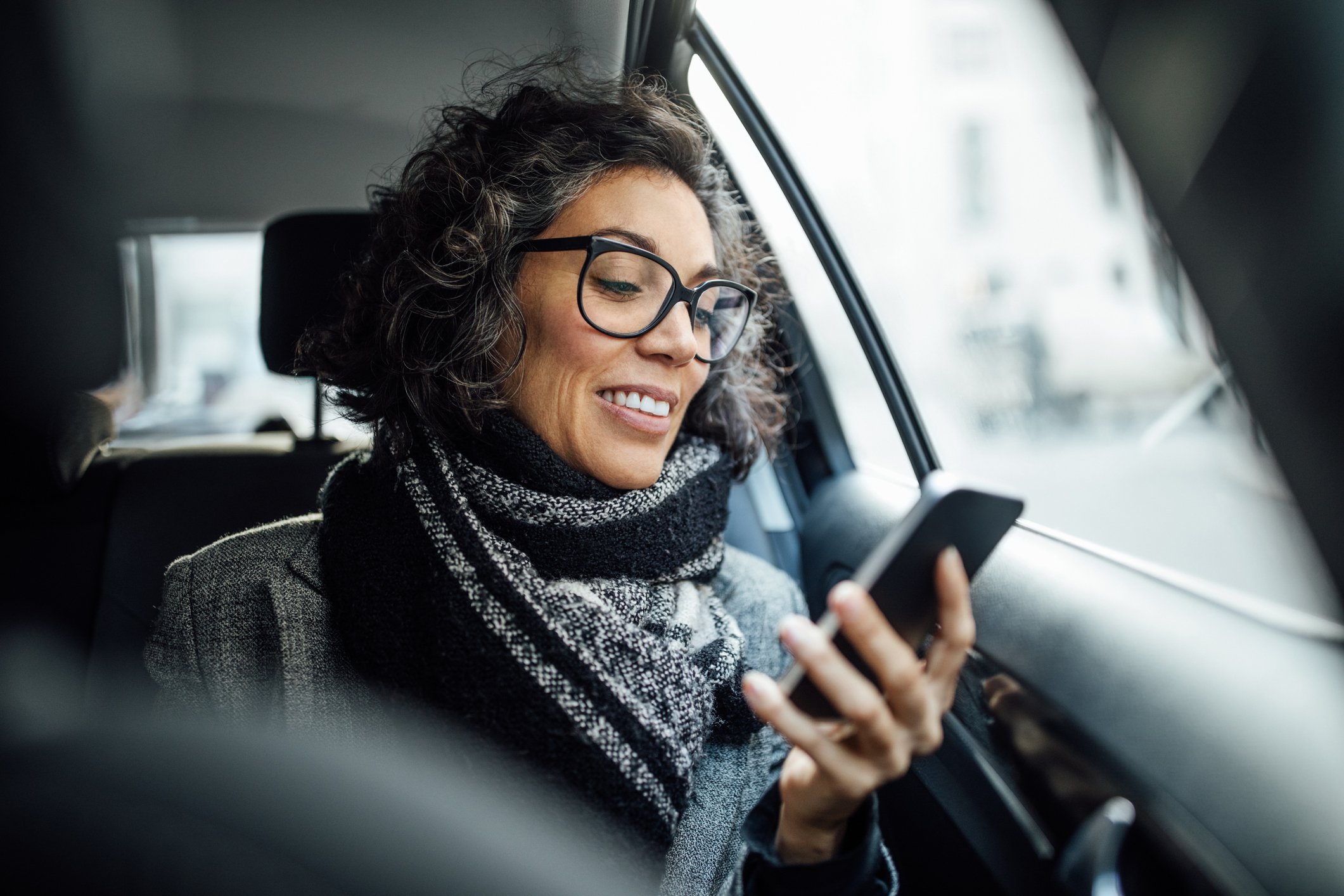 A woman sitting in a car and looking at her mobile phone.