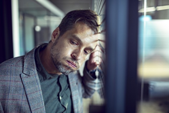 A man leaning against a window dissapointed.