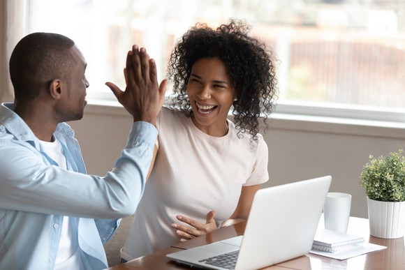 Two people giving each other a high five while sitting in front of a laptop.