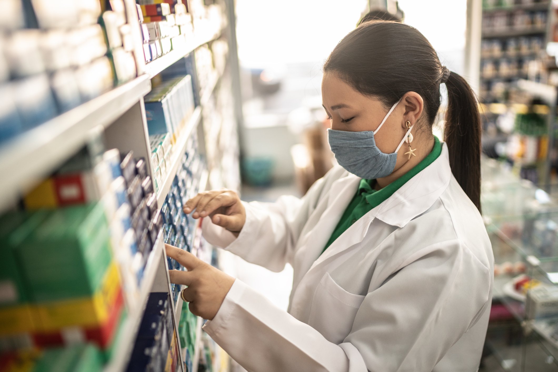 A pharmacist looks at boxes of medication while behind the counter in the pharmacy.