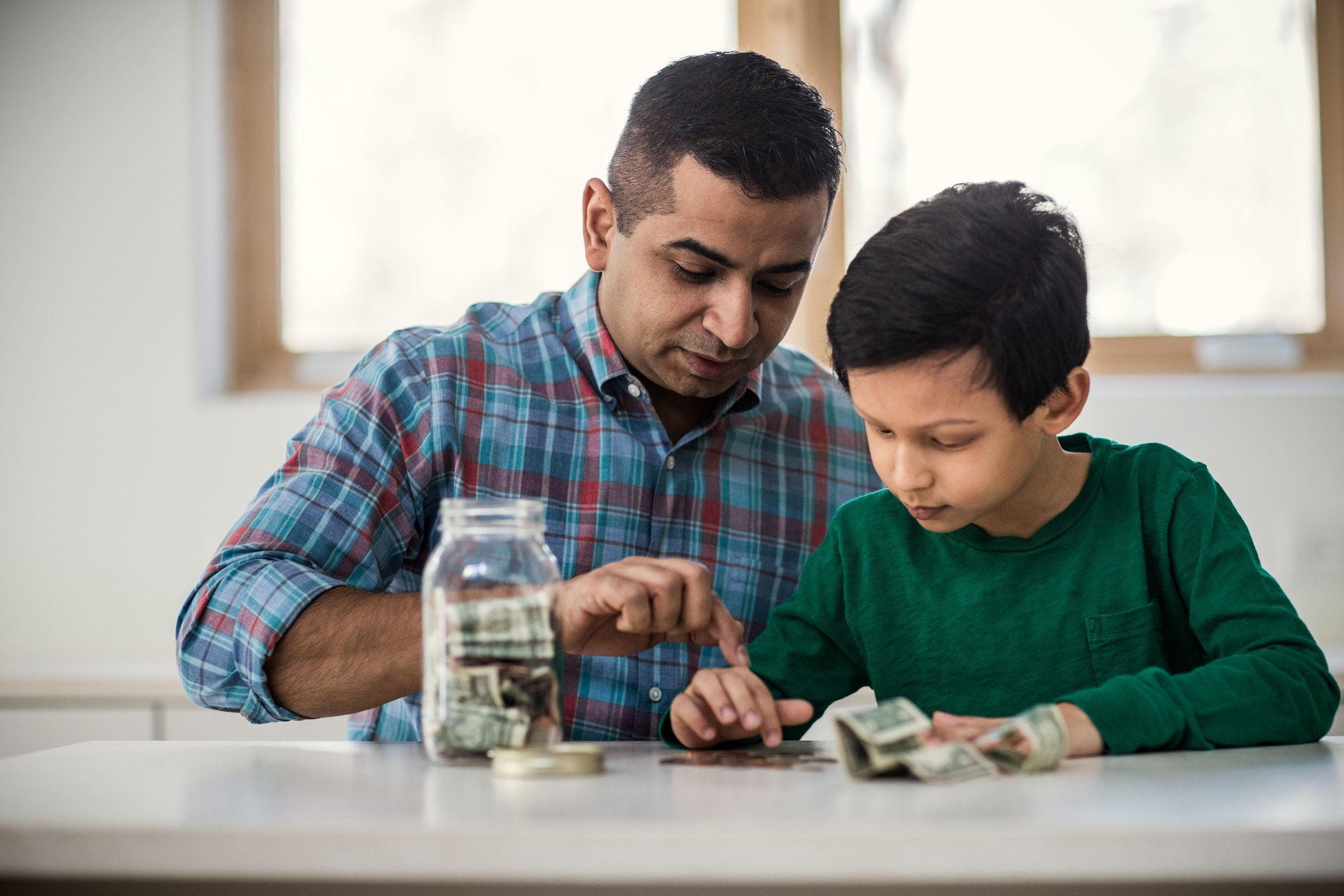An adult and child counting money on a table.