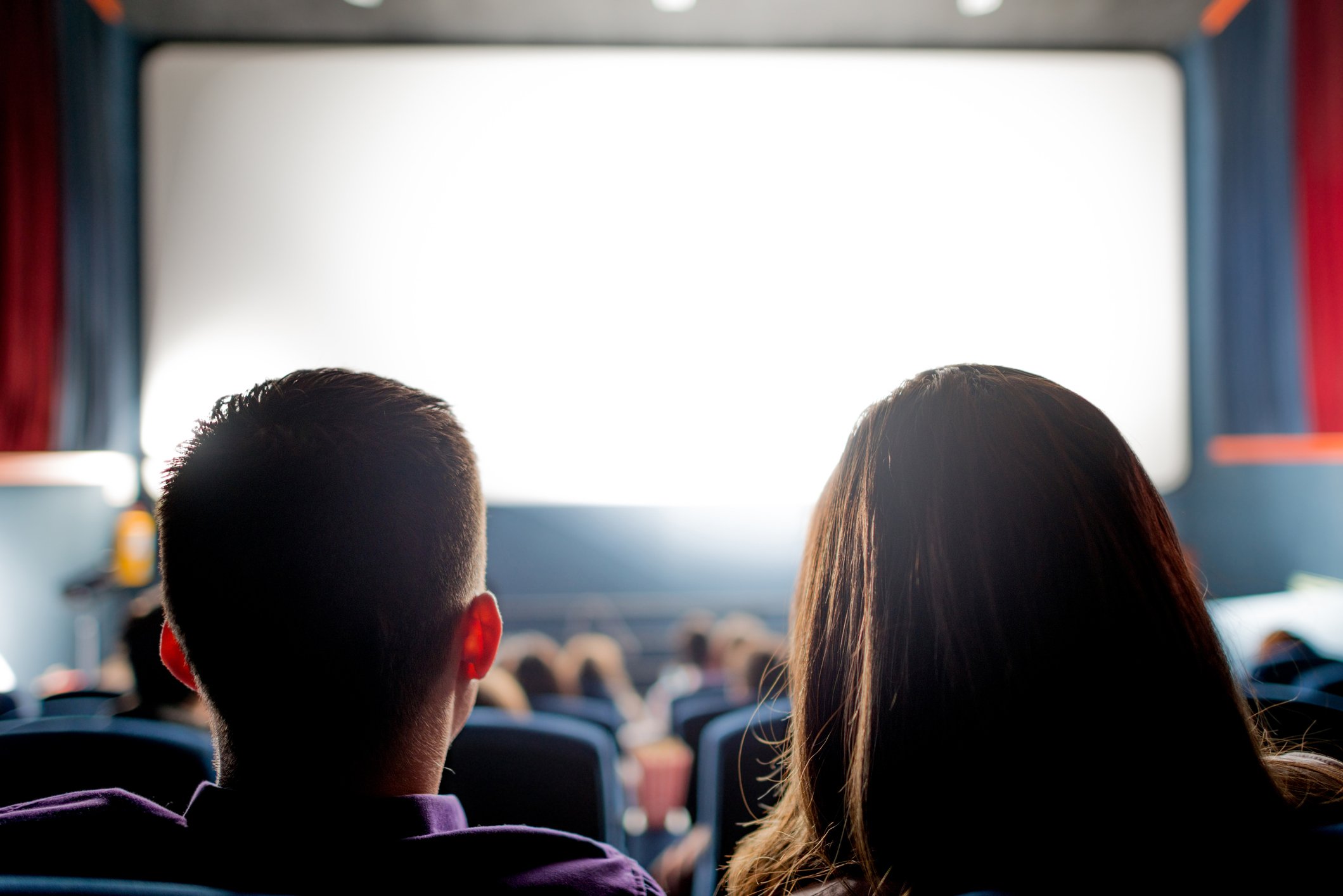 View of blank movie screen from back of a crowded theater. 