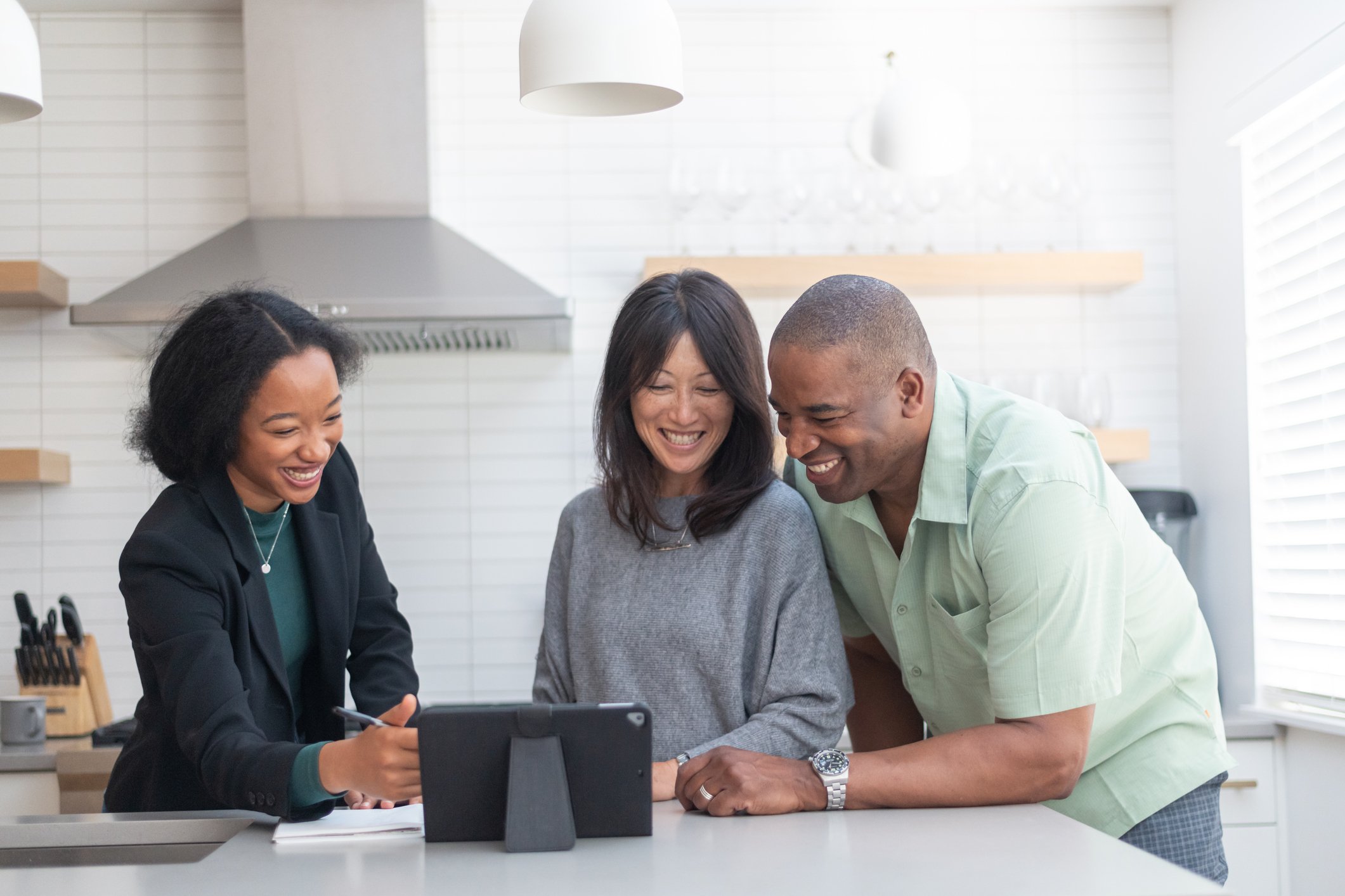 Group of people standing at a kitchen counter looking at a tablet.