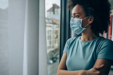 person wearing a mask looking out a window