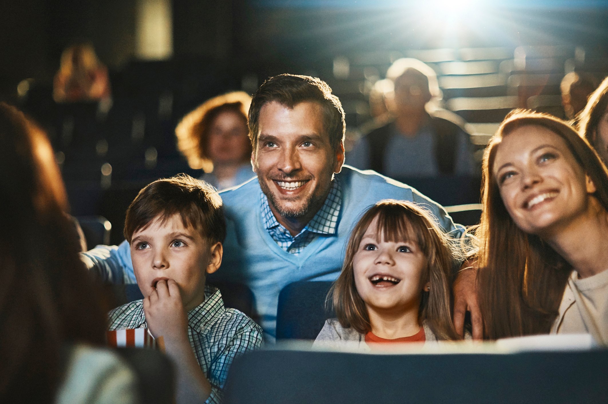 A happy family at the movies with other cinema-goers visible in the seats behind them.