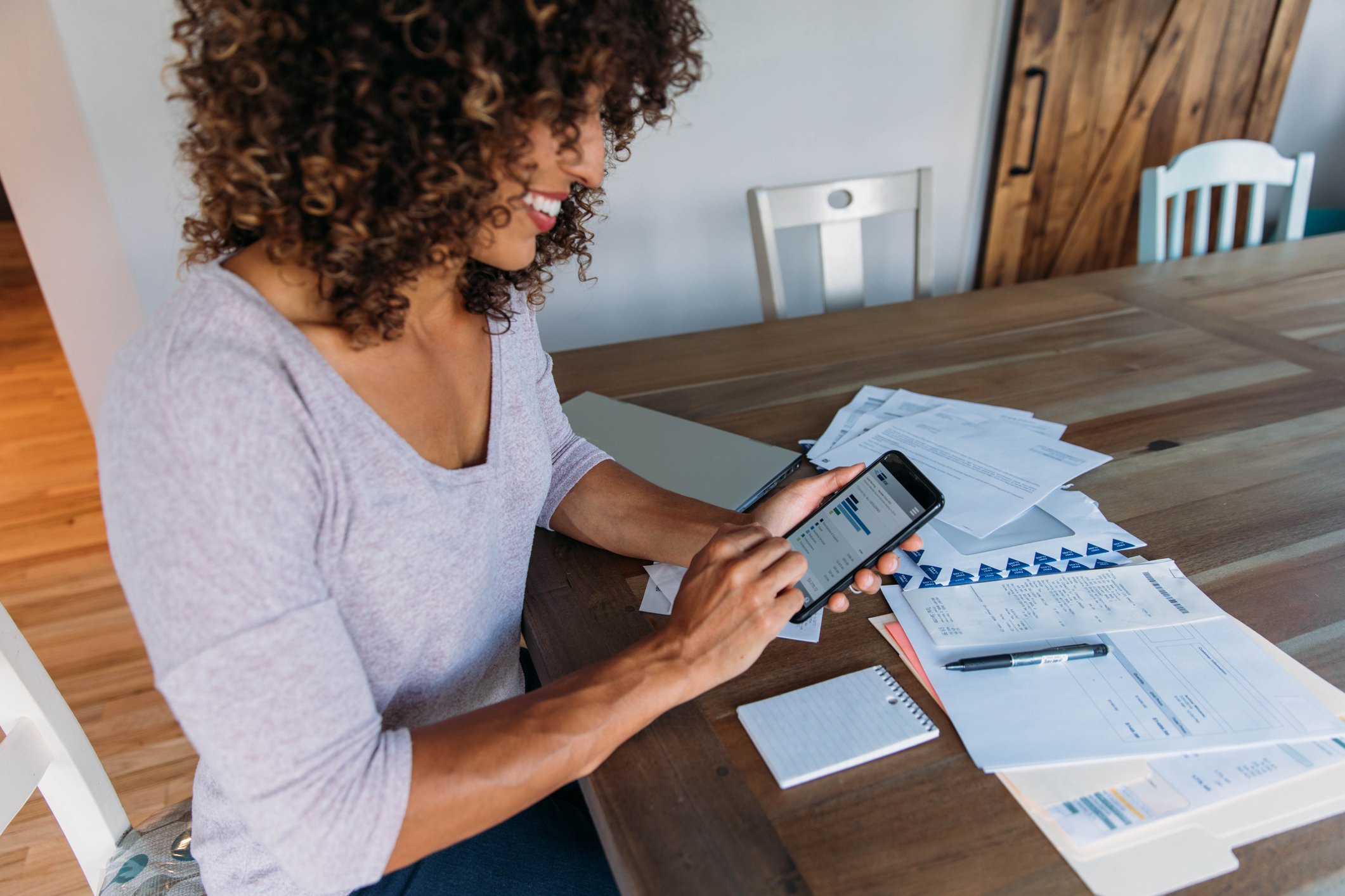 A homeowner pays bills on a smartphone at the dining room table.