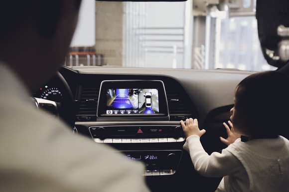 An adult and a child look at a dashboard screen in a vehicle that shows what is behind the vehicle using cameras