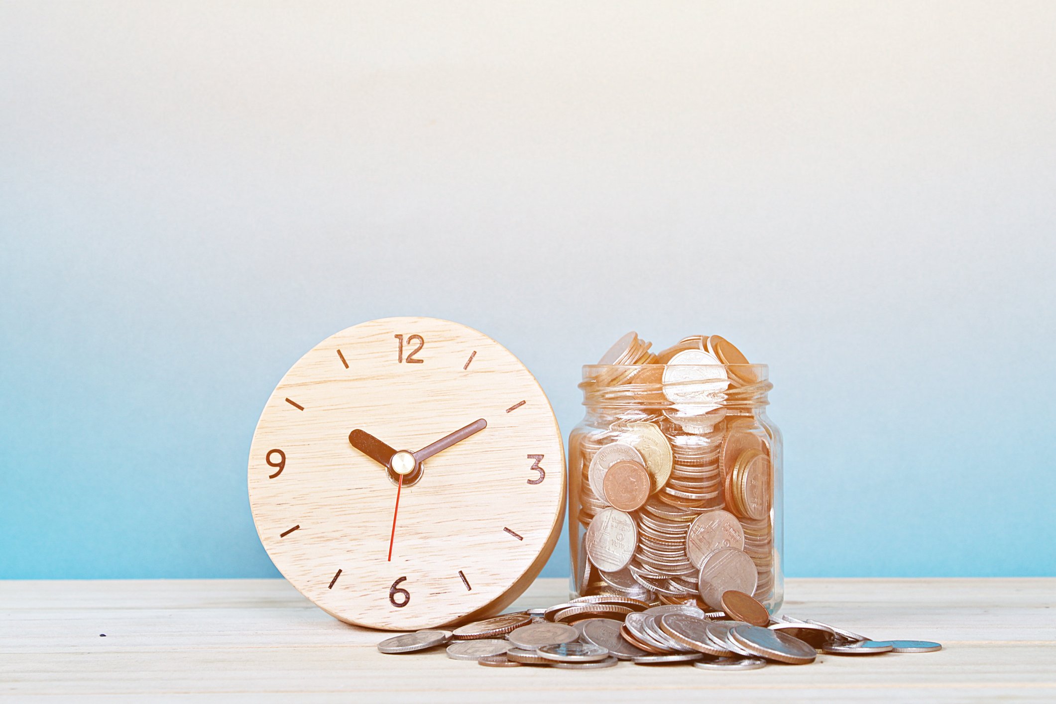 A clock next to a jar of coins.
