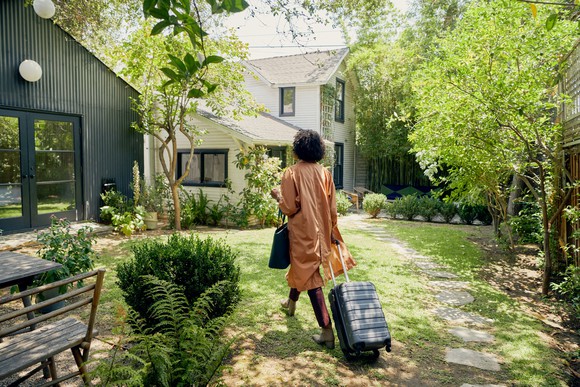 An individual pulling a suitcase and walking toward a house.