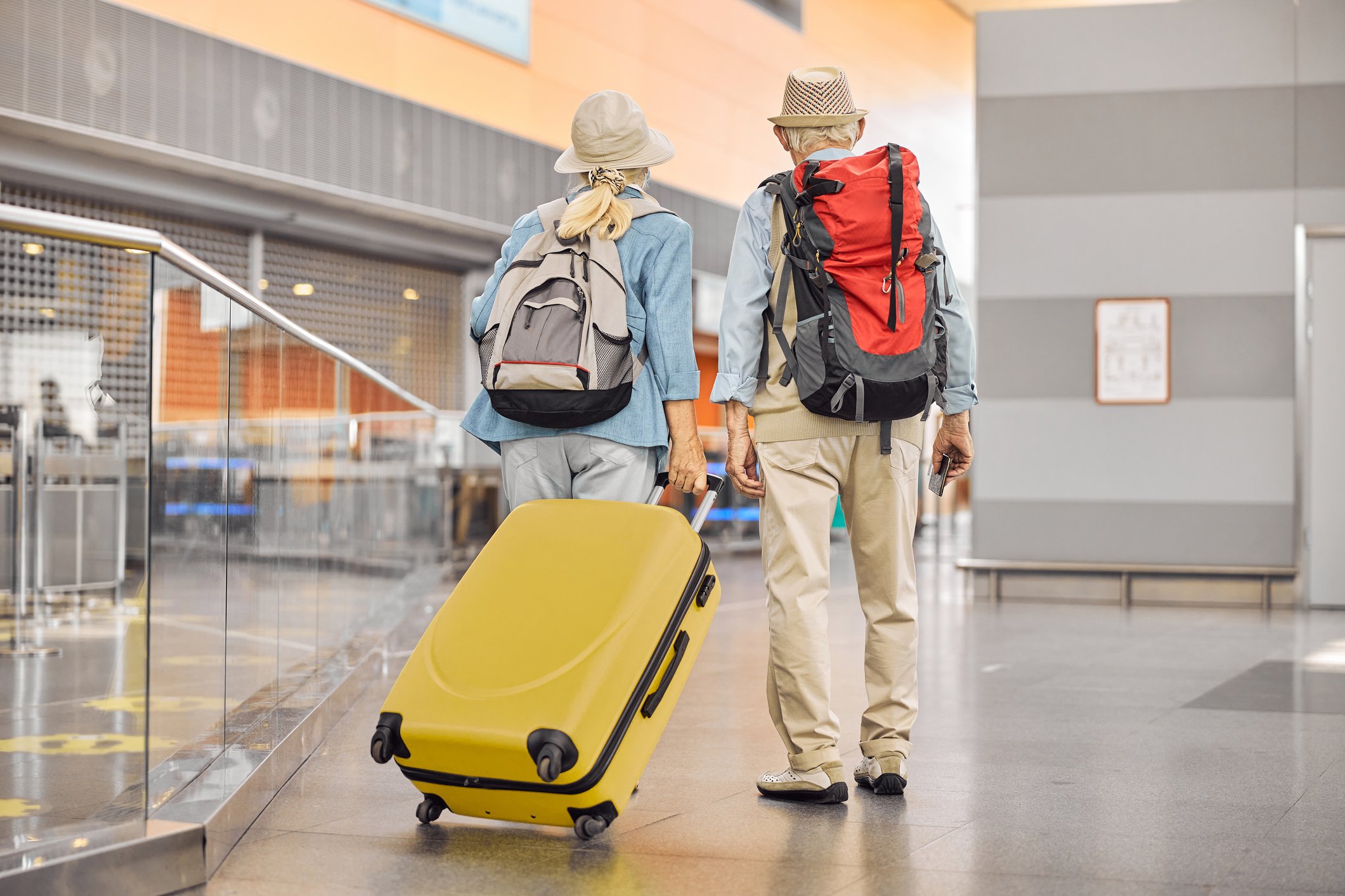 Two people walking through an airport with bags. 