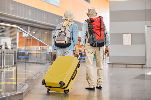 Two people walking through an airport with bags. 
