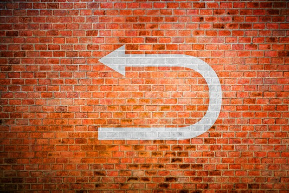 A white backward-curving arrow painted on a red brick wall. 