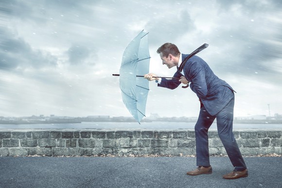 A business man holds out a light blue umbrella to brace against a strong headwind. 
