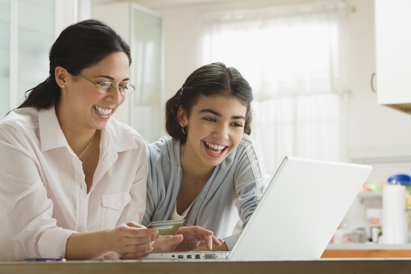 Adult and teenager smile while shopping online using a laptop.