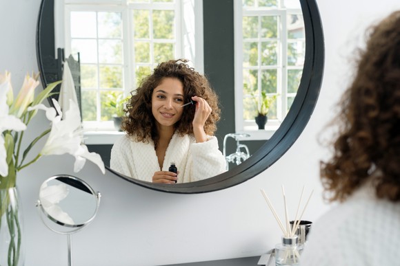Person looking into a mirror and applying a skin serum.
