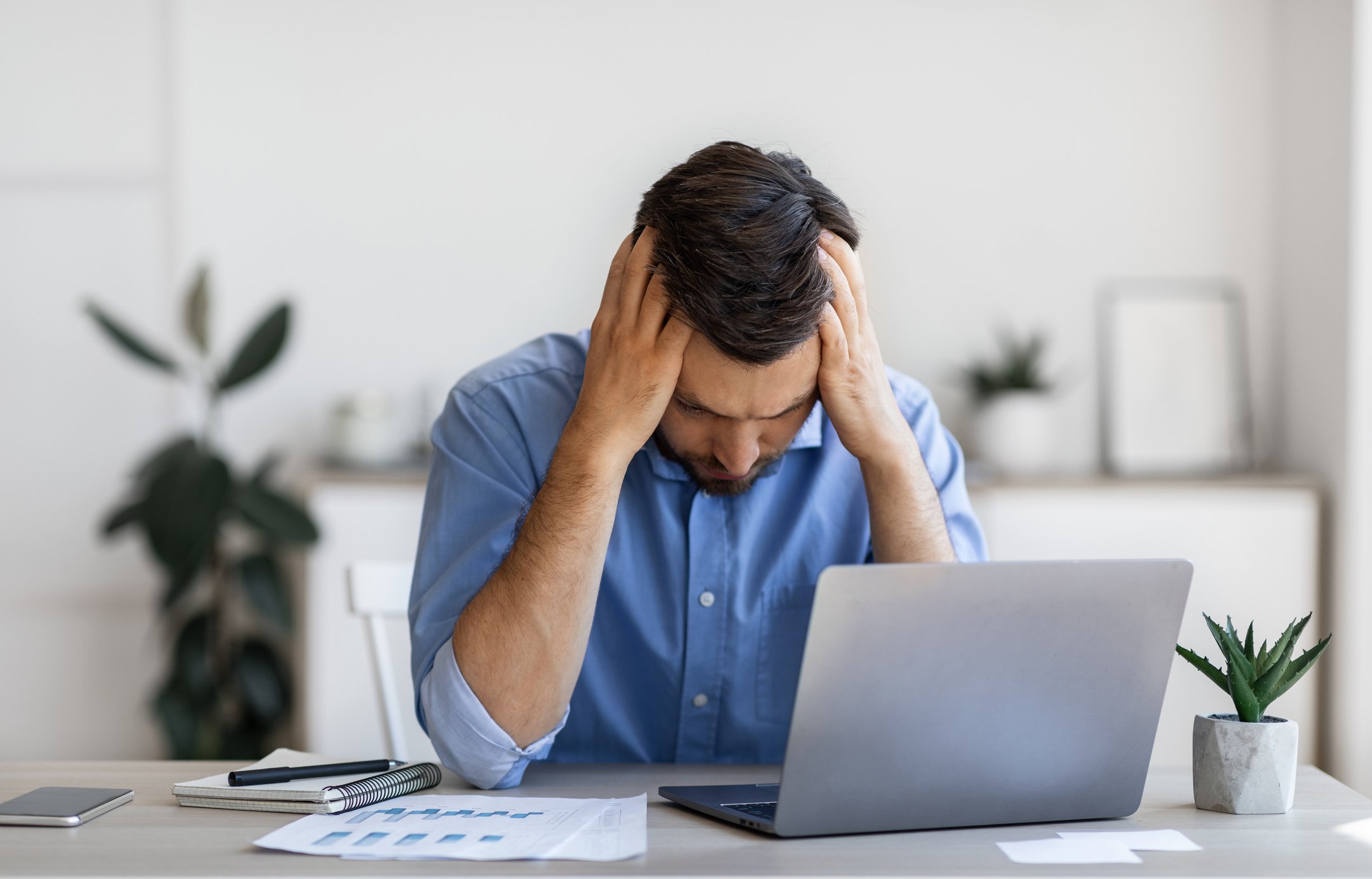 A man holds his head while working with a laptop.