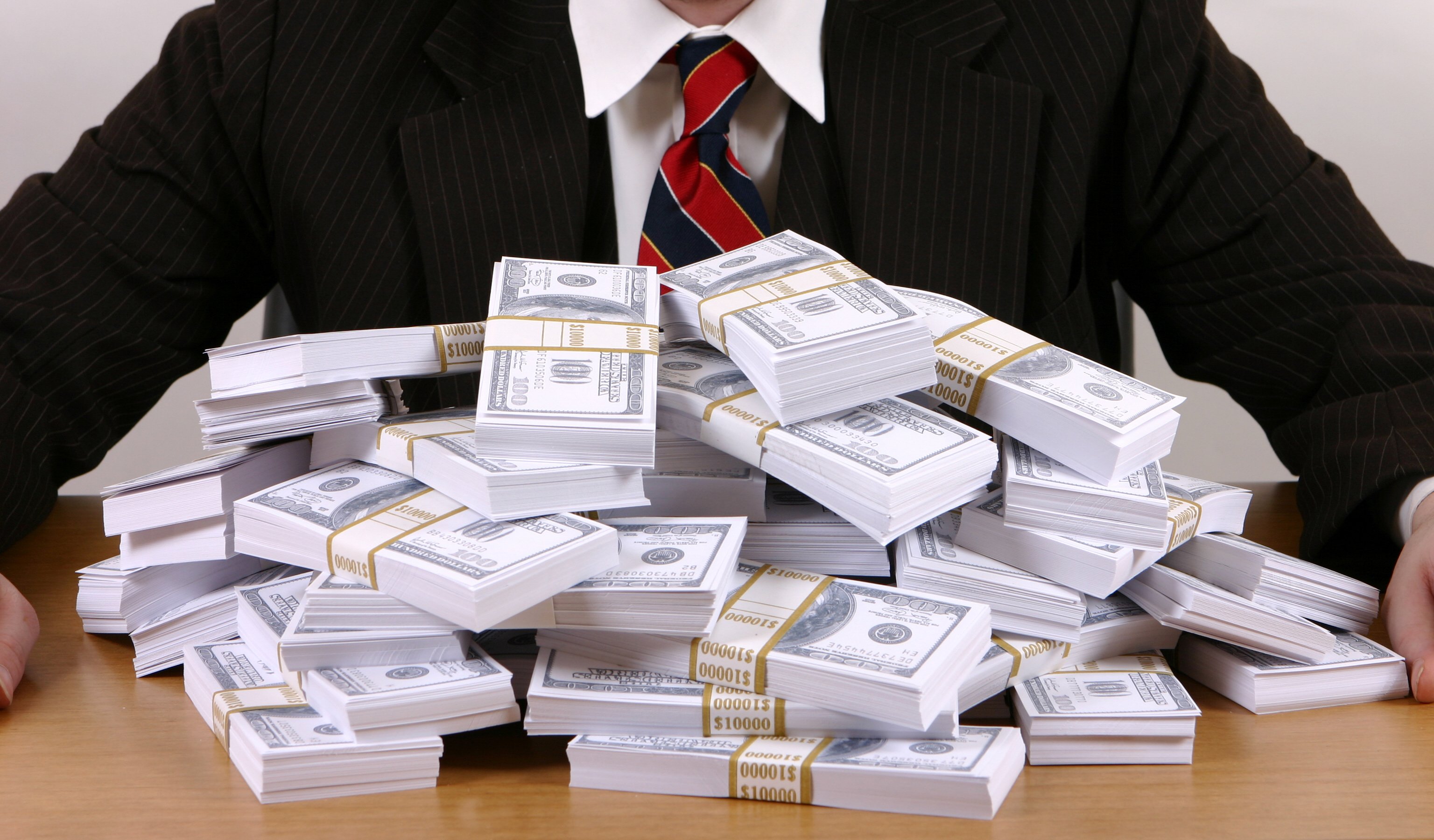 Person in business suit sitting in front of wads of money.