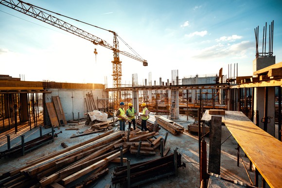 Workers at a high-rise construction site against a bright sky. 