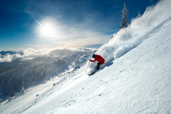 Person skiing downhill on a mountain is making trail of powder.