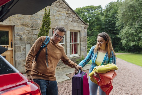 Two people unpacking luggage out of a car.