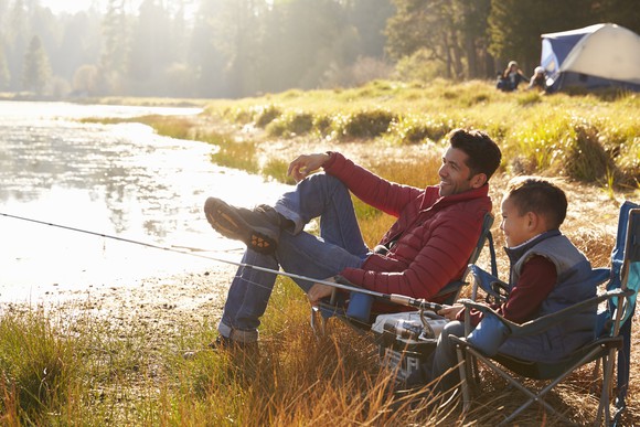 Adult and child fishing at a stream, with a tent set up in the background.