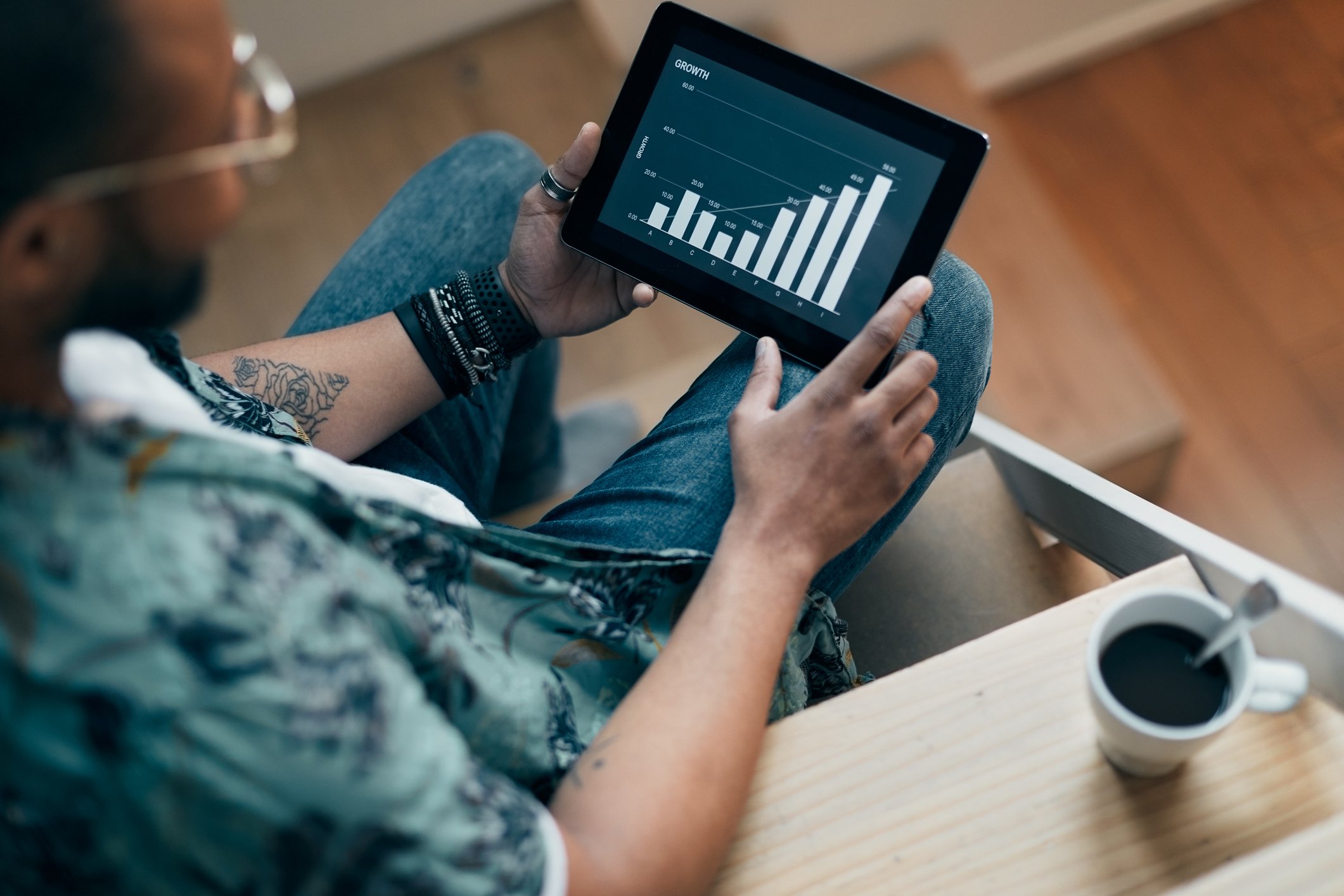 A man sitting on stairs holds a tablet computer and looks at a screen showing a bar chart