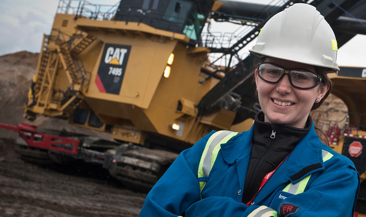A female employee of Caterpillar, wearing a hardhat, stands in front of some Caterpillar mining equipment