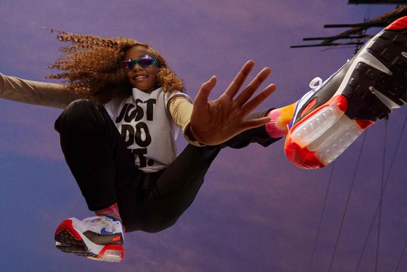 A young woman wearing sunglasses and a Just Do It t-shirt strikes an athletic pose while wearing Nike shoes