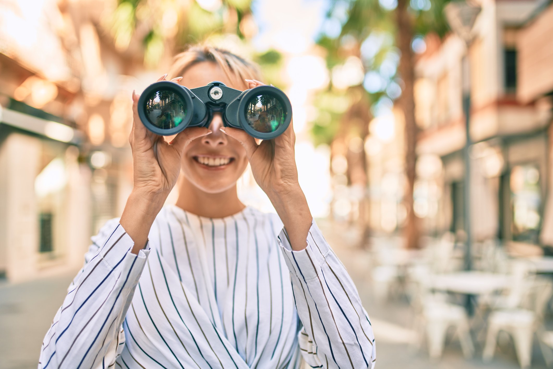 A smiling person using binoculars.