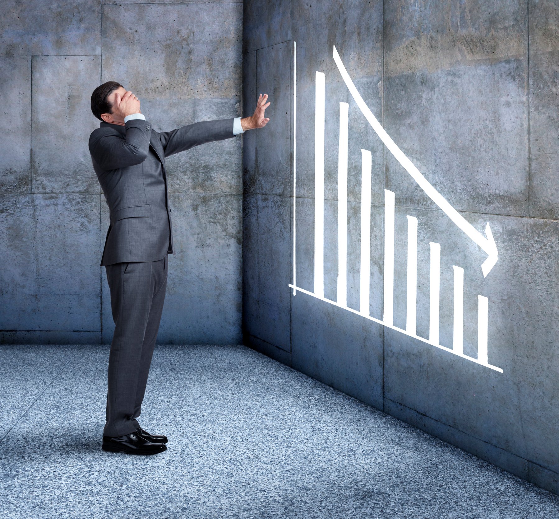 A businessperson covering their face in front of a downward-trending graph.