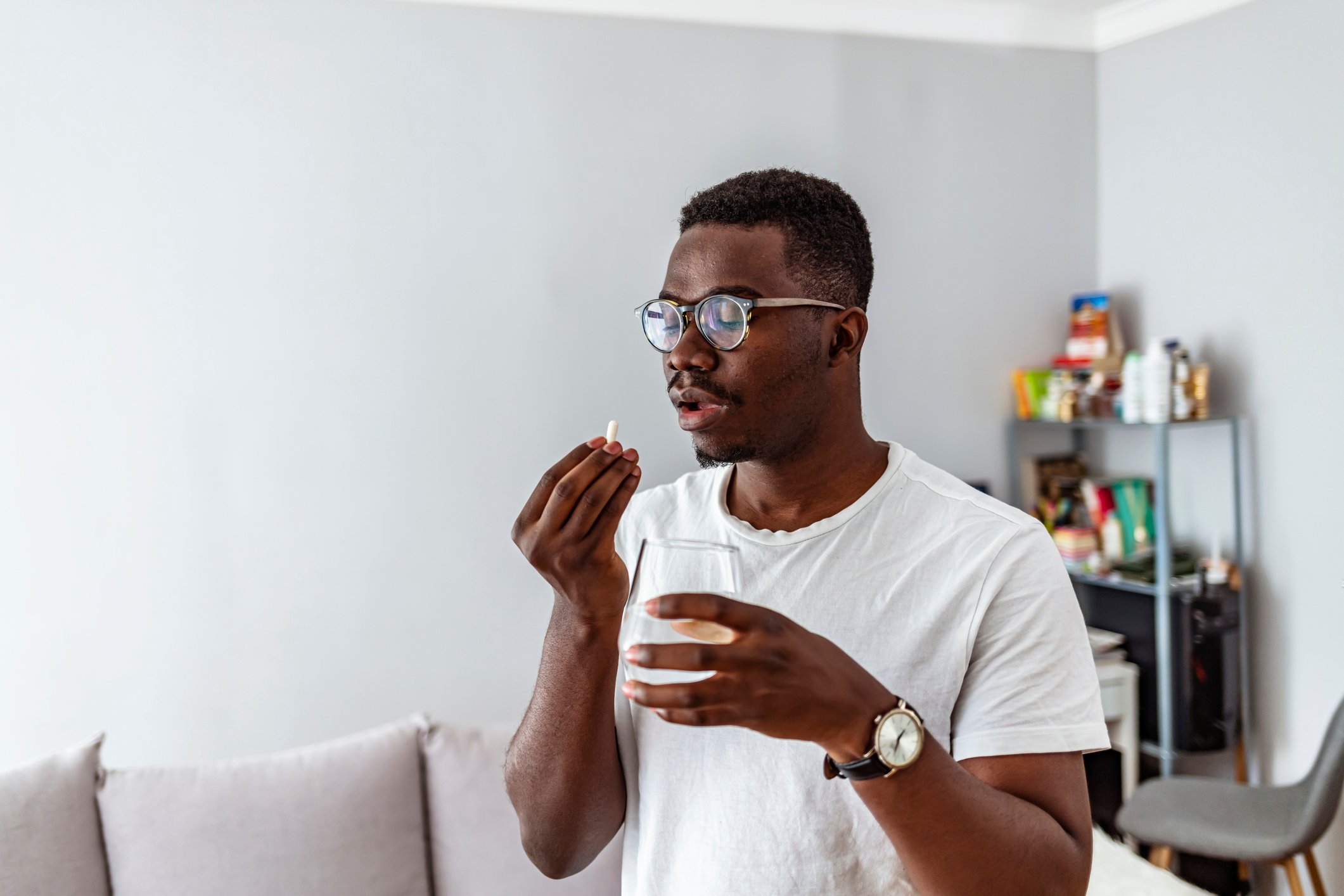 Patient taking a pill in a room with gray walls, a gray couch, and a shelf in the background. 