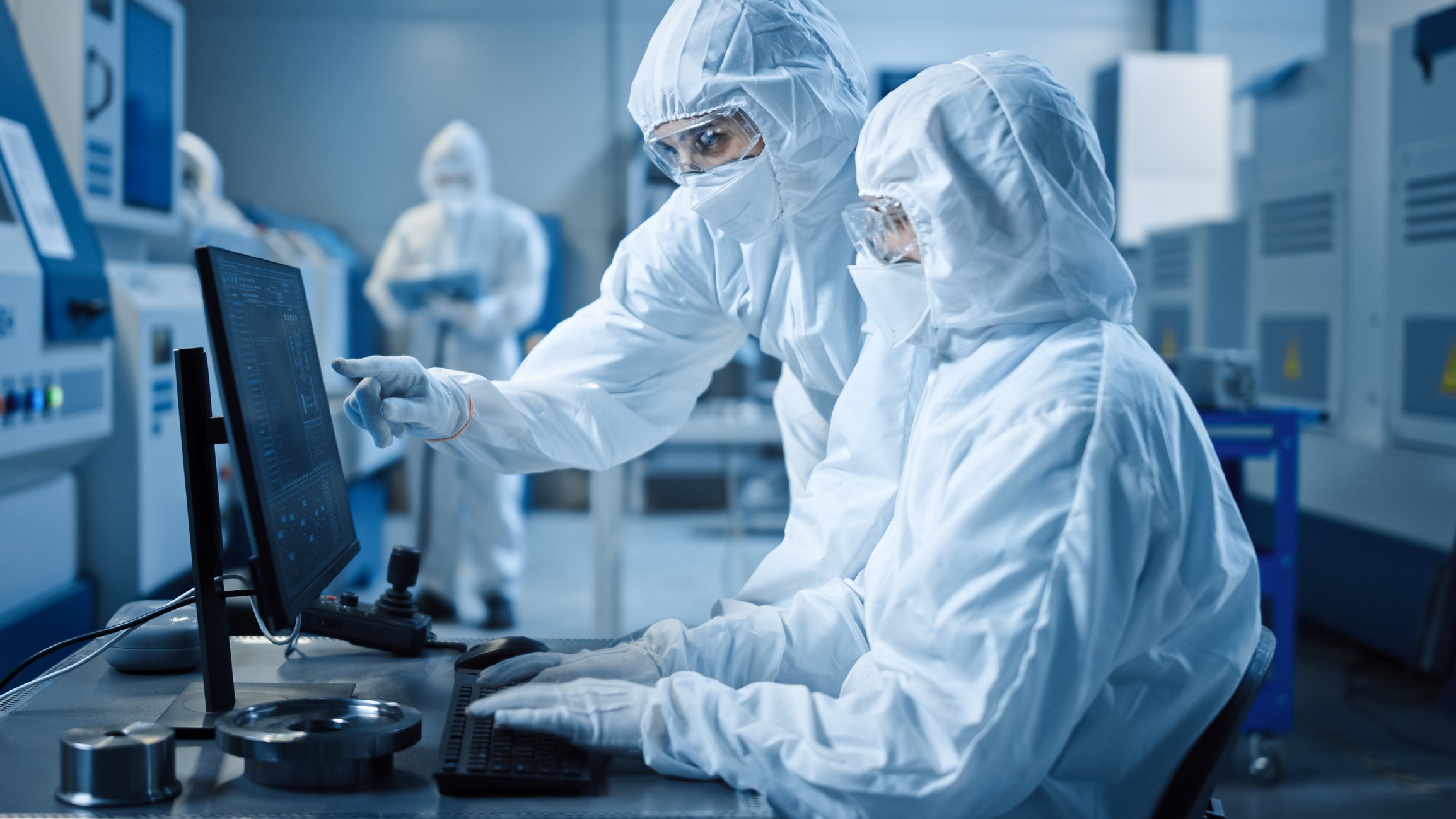 Researchers looking at a monitor in a cleanroom.