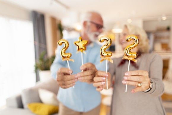 Two people each holding two gold foil balloons that say 2022 with the zero represented by a star balloon.