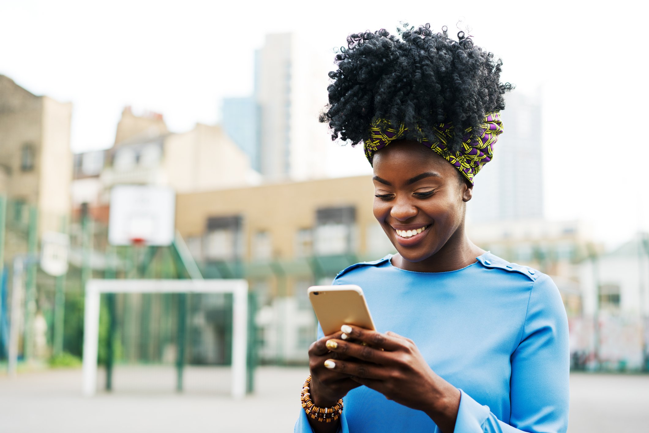 Young adult smiles while looking at smartphone outside.
