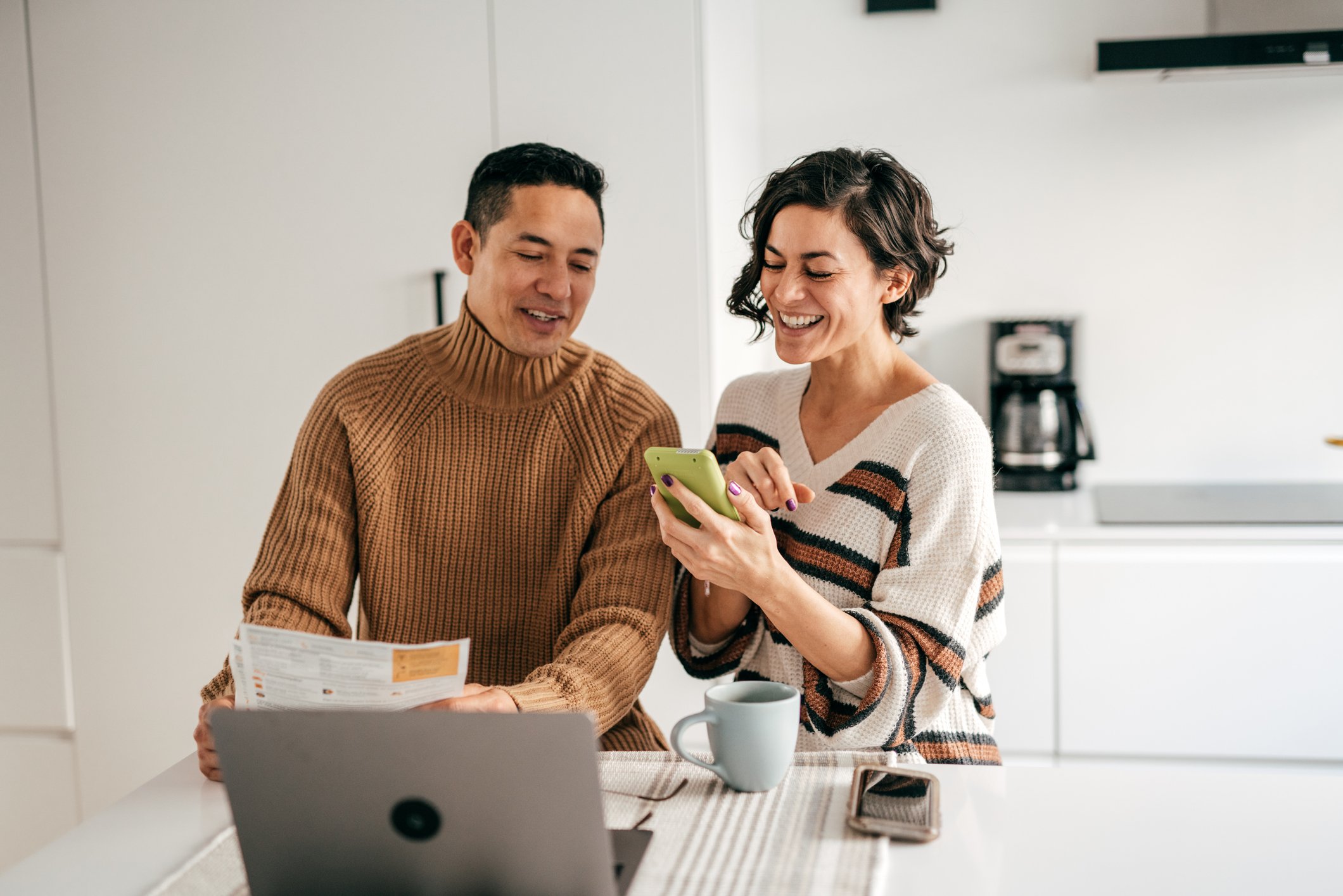Two people standing at a countertop with a laptop and phone, checking numbers on new investments.