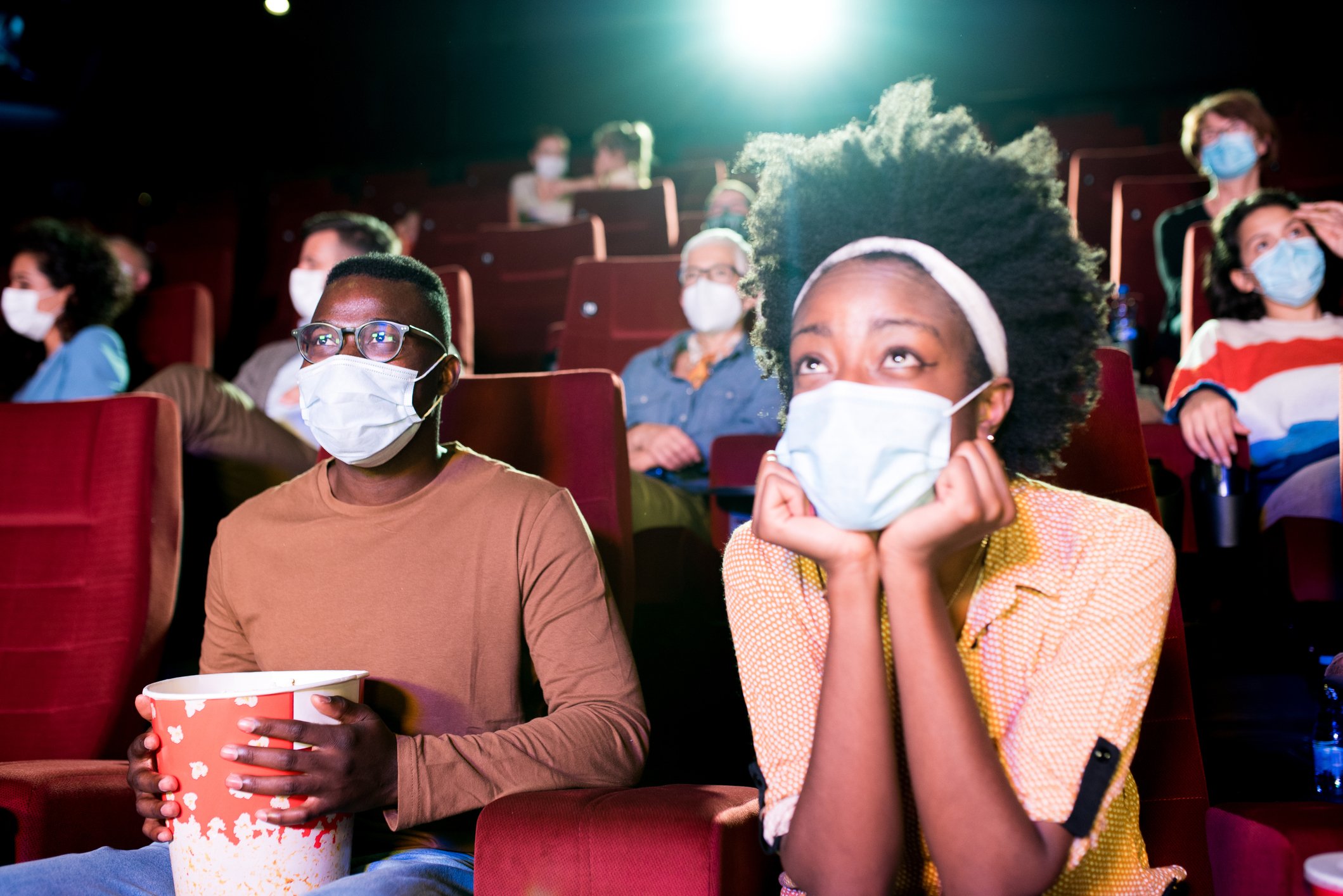 Masked moviegoers stare intensely at a movie screen in a theater.