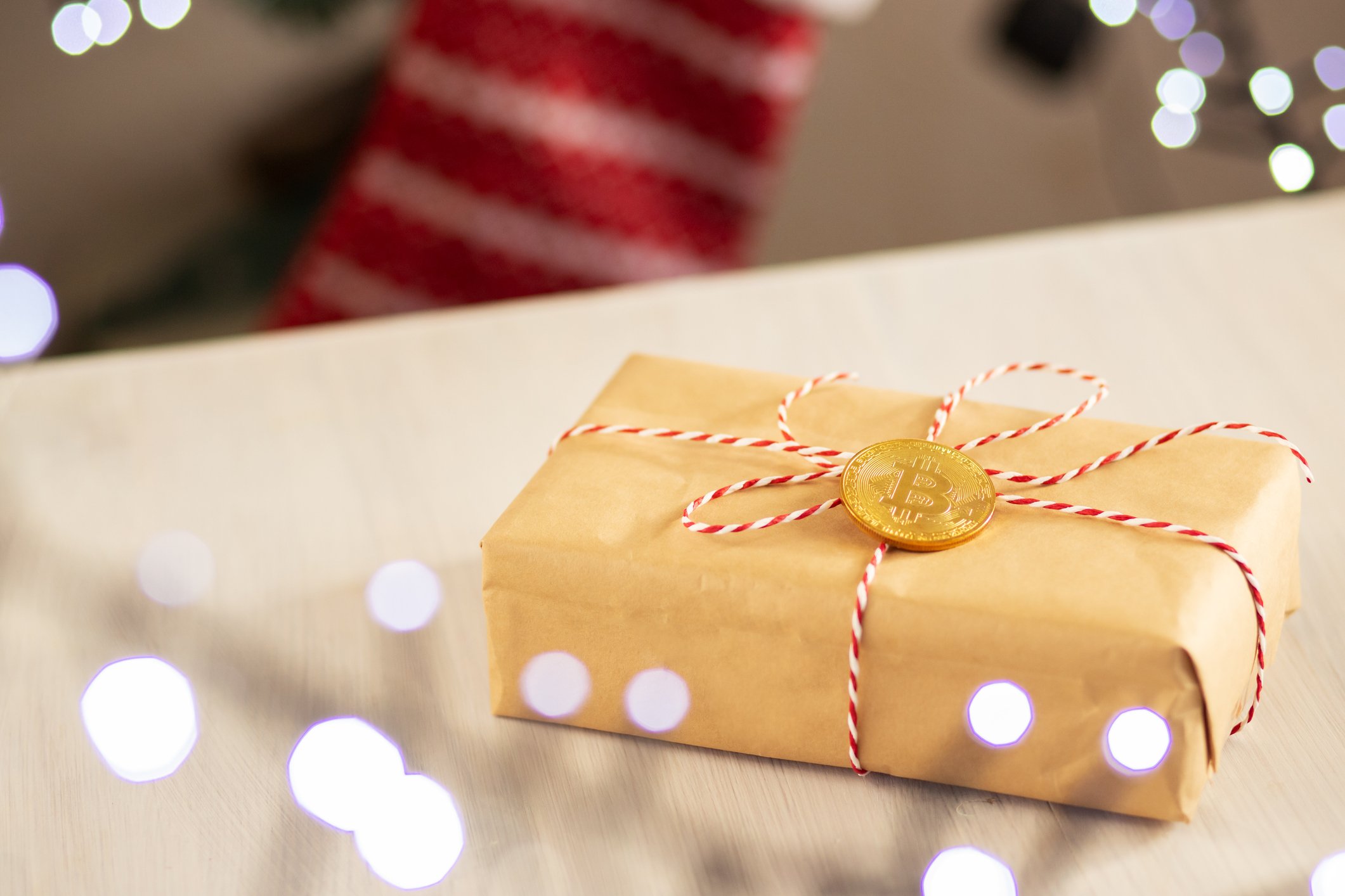 A wrapped present with a gold bitcoin tied to the top of the box.