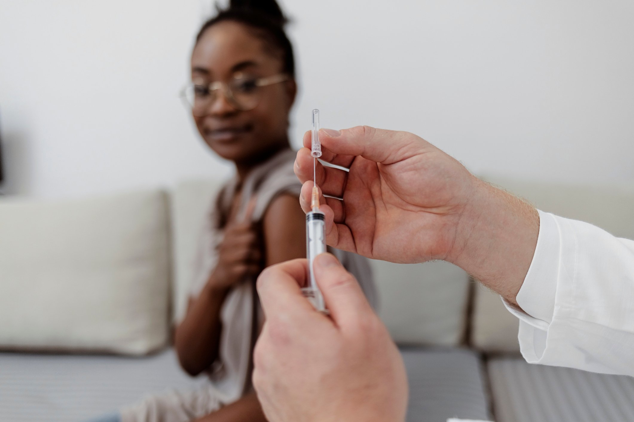 A doctor loads a syringe while a patient waits with her sleeve pulled up.