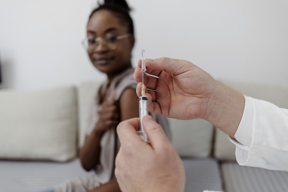A doctor loads a syringe while a patient waits with her sleeve pulled up.
