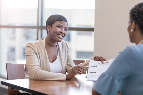 A person sitting at a desk and showing a document to another person. 