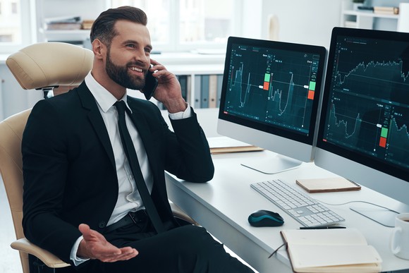Investor talking on the phone while reviewing charts on two computer screens.